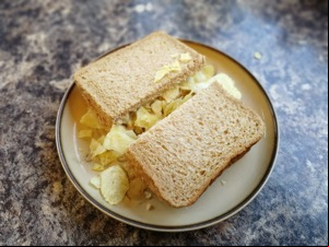 Halved brown bread sandwich over-filled with crisps