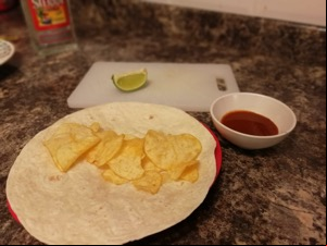 Crisps on an open wrap alongside lime and sauce