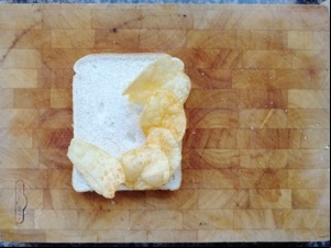 Five crisps on white bread on a chopping board